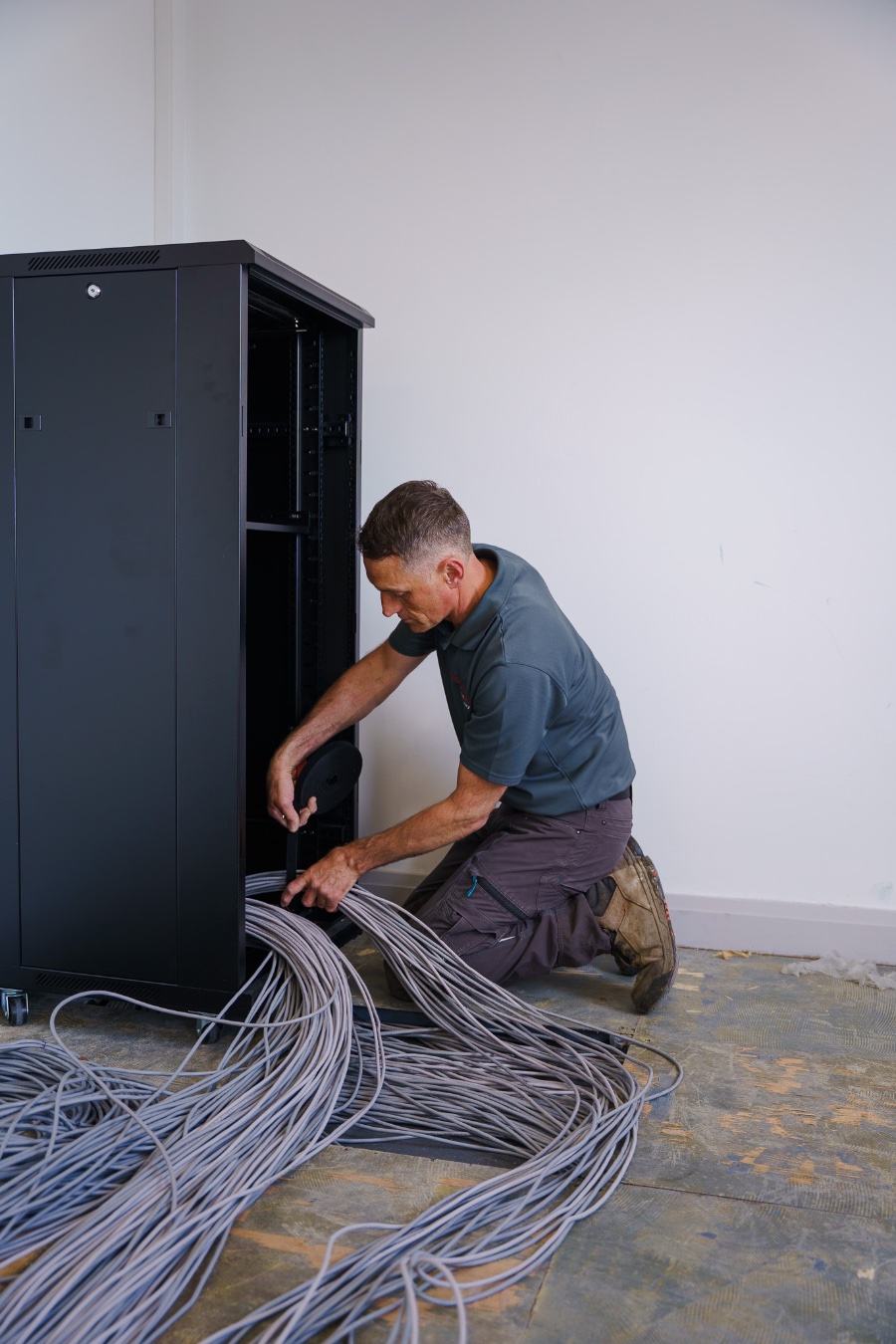 A Fibretech engineer feeding data cabling into a comms cabinet